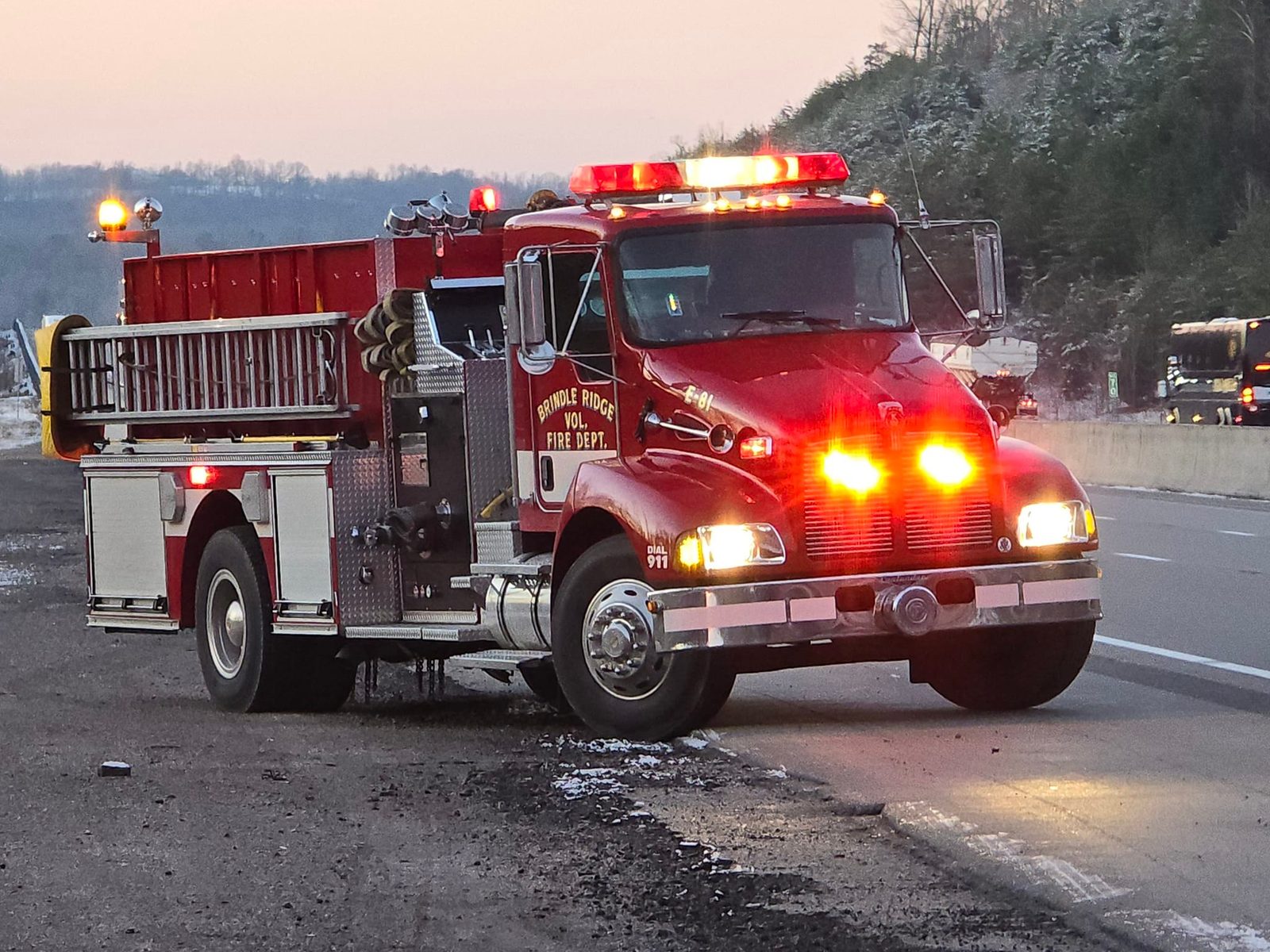 Engine 81, a red Kenworth pumper with emergency lights on, parked on a highway shoulder at dusk in winter