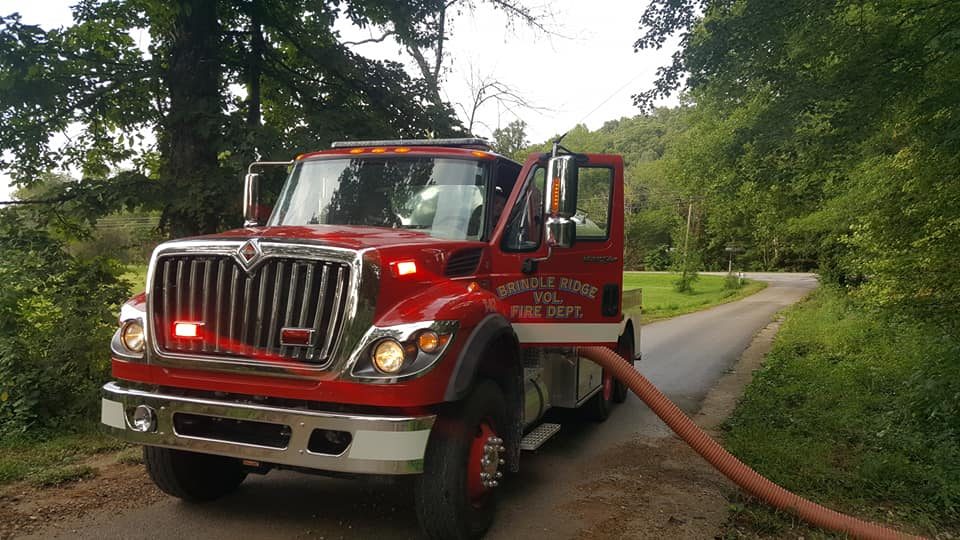 Tanker 82, a red International vacuum tanker on a narrow rural road with a hard suction hose run out behind it
